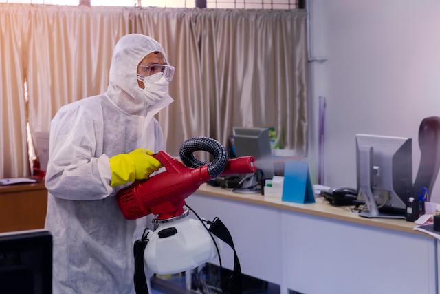 A custodial worker using an electrostatic mister to clean an office. 