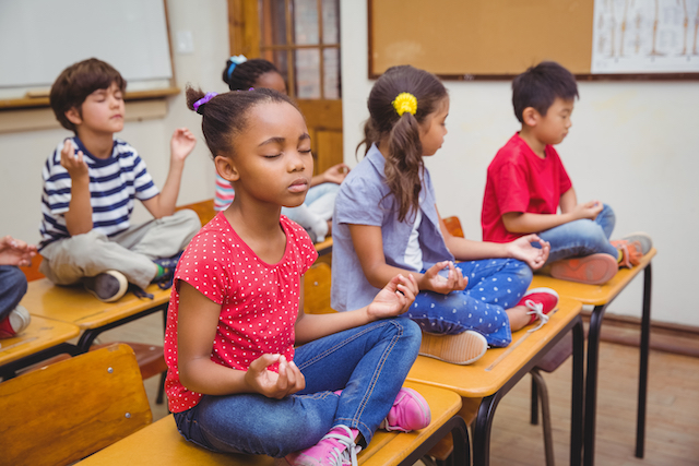 Children meditating in a classroom. 