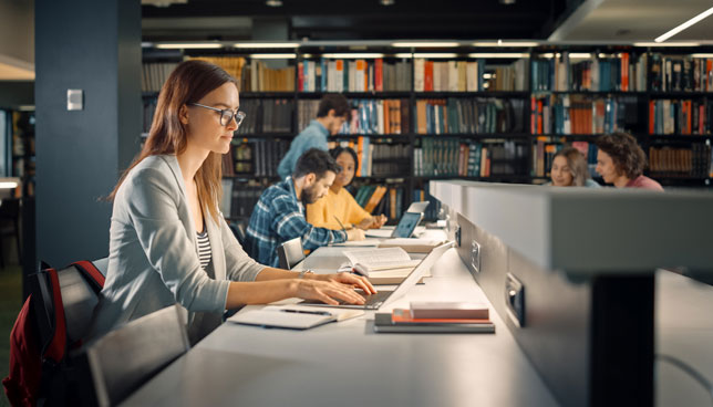 Girl Sitting at Library Desk, Using Laptop