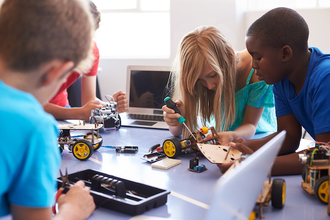 Children using tools like a screwdriver to tinker with a robot on a table. 